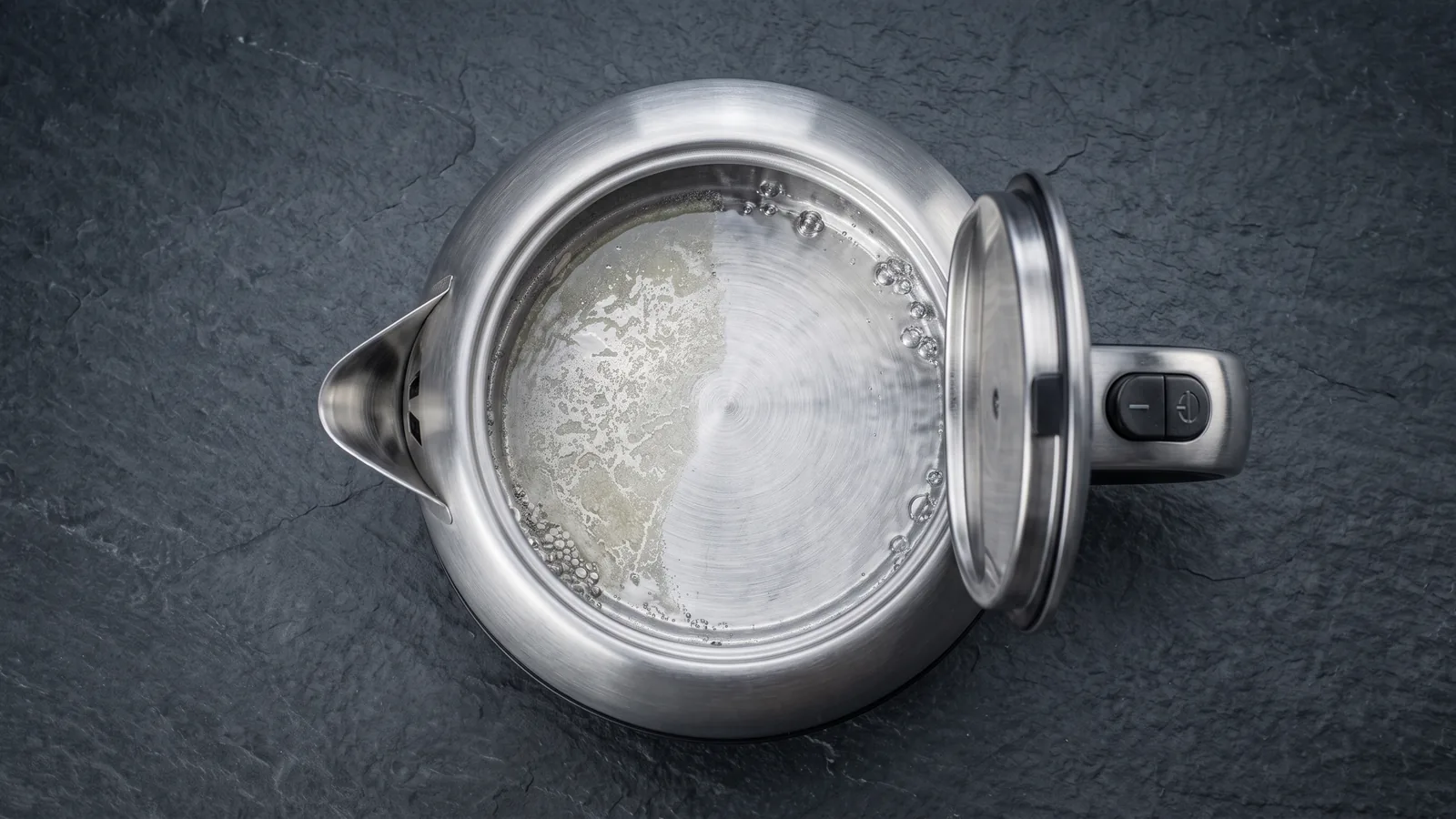 The interior of an electric kettle with clear water gently effervescing against pale limescale, bright clean metal emerging, a descaling-in-progress feel.